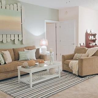 A cozy and elegantly designed living room featuring a comfortable sofa set, a coffee table on a striped rug, subtle artwork, and soft lighting.