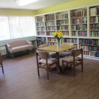A cozy library reading room with bookshelves, a round table, and a sofa.