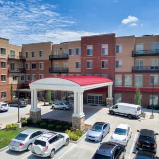 A view of a multi-story building with a red and white entrance awning, surrounded by a parking lot filled with cars.