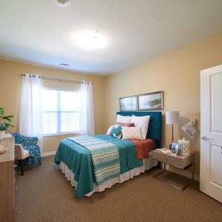 A cozy bedroom with teal and white bedding, complemented by neatly arranged furniture and decor.
