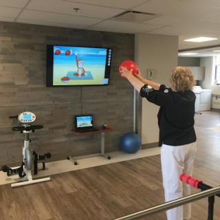 A woman engaging in a digital rehabilitation exercise using handheld weights while interacting with a video game on the screen.