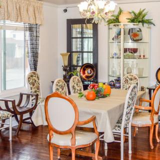A well-decorated dining room featuring a table with a fruit bowl, surrounded by chairs and illuminated by a chandelier.