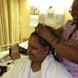 A woman getting her hair braided in a salon setting, smiling as she enjoys the service.