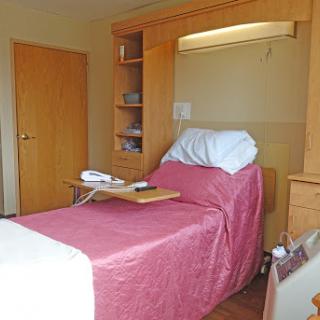 A cozy and functional hospital patient room featuring a bed, bedside table, and storage.