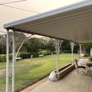 A covered patio with outdoor seating overlooks a well-maintained garden and lawn.