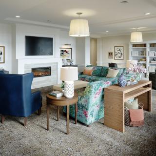A cozy living room featuring a floral sofa, blue armchairs, and a fireplace with a mounted television.