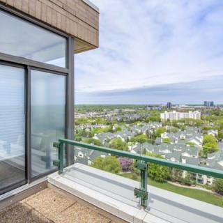 A balcony view showcasing a cityscape with greenery and distant buildings under a blue sky.