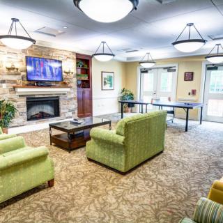 A cozy living room with green sofas, a television mounted above a fireplace, and elegant chandeliers.