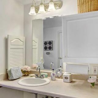 A neatly organized bathroom with a sink, mirror, and overhead lighting.