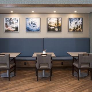 A modern dining area in a restaurant featuring tables and chairs, with artwork on the walls and subtle lighting.