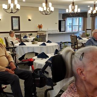 A group of elderly individuals gathered in a dining room with chandeliers overhead.