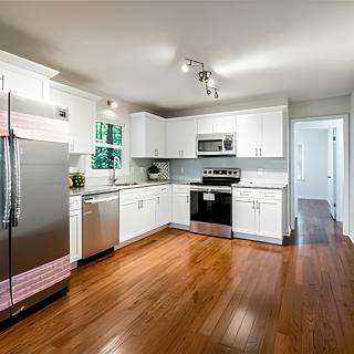 A modern kitchen with white cabinets and stainless steel appliances on a hardwood floor.