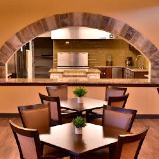 A cozy restaurant interior featuring several dining tables with a view into the kitchen through a large archway.