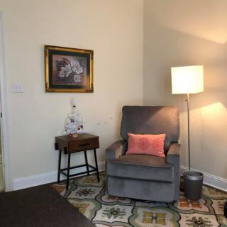 A cozy corner of a living room featuring a gray armchair with a pink cushion, accompanied by a floor lamp and side table, and adorned with wall art.