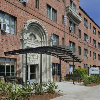 Entrance of a brick apartment building with a metal canopy and landscaped surroundings.