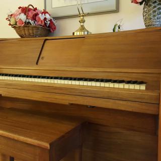 A wooden piano with a decorative floral arrangement on top, accompanied by a matching bench.