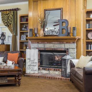 A cozy living room with a central fireplace, surrounded by decor and bookshelves.