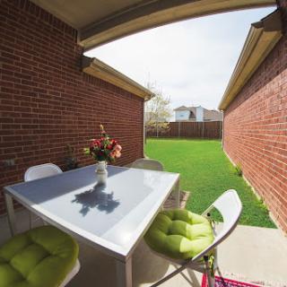 A cozy outdoor patio area featuring a modern table and stylish seating, surrounded by brick walls and a lush green lawn.
