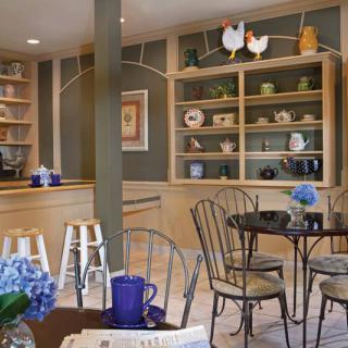 A cozy cafe with elegant interior design, featuring tables and chairs surrounded by decorative shelves and flowers.