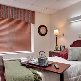 A cozy hospital room featuring a neatly made bed, a bedside table with a tray, and warm lighting.
