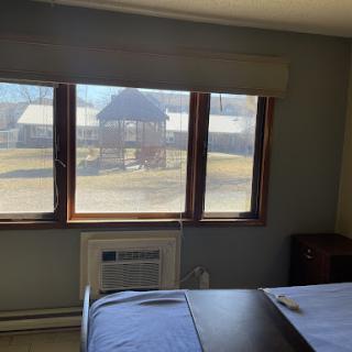 A cozy room featuring a large window with a view outside, an air conditioning unit, and simple furnishings.