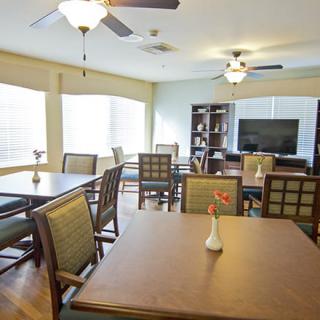 A well-lit dining area featuring tables and chairs, ceiling fans, and a vase with flowers on one of the tables.