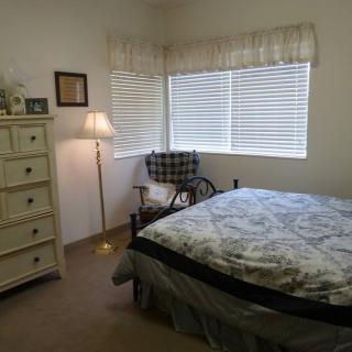 A cozy bedroom with a bed, dresser, chair, and lamp by the window.