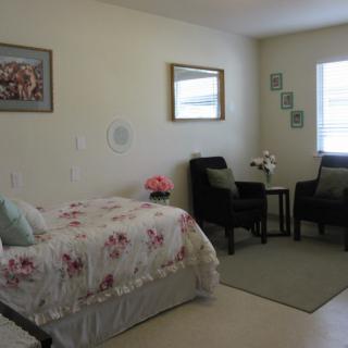 A cozy bedroom with a floral bedspread, two chairs, and soft lighting.