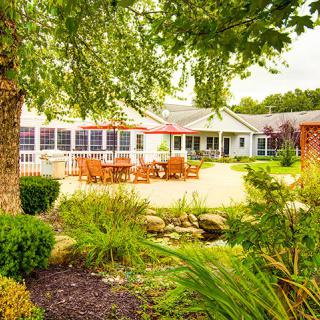 A beautifully landscaped garden featuring a patio with outdoor furniture, surrounded by lush greenery and trees.