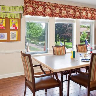 A well-lit dining area with a table and chairs set, featuring large windows and a view of the outside.