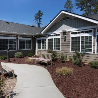 A well-maintained residential house exterior with a landscaped front yard and two benches along the pathway.