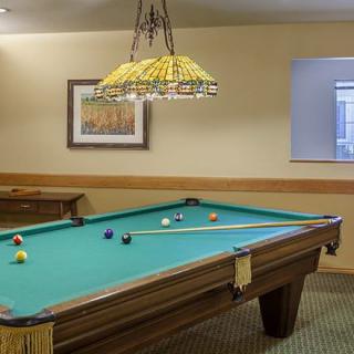 A cozy recreation room featuring a billiards table with cue sticks arranged on top, under a decorative hanging lamp.