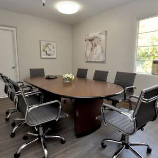 A modern conference room with a large wooden meeting table, surrounded by sleek office chairs and adorned with artwork on the walls.
