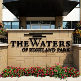 Entrance sign for The Waters of Highland Park, featuring landscaping with flowers.