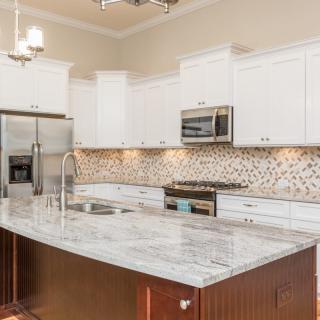 A modern kitchen featuring white cabinets, stainless steel appliances, and a large island with a marble countertop.