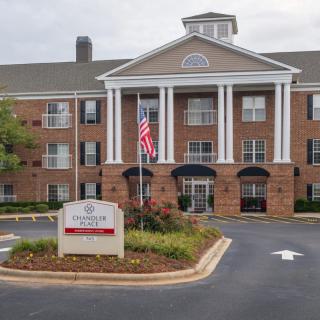 A brick retirement home with a classical design, featuring white columns and an American flag at the entrance.