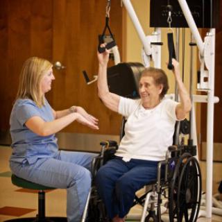 A healthcare professional assists an elderly patient in a physical therapy session, using specialized equipment to promote rehabilitation.