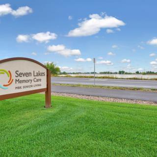 A sign for Seven Lakes Memory Care set against a clear blue sky with scattered clouds.