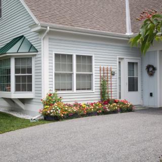 A charming house with a well-maintained flower garden and a driveway leading to the front door.