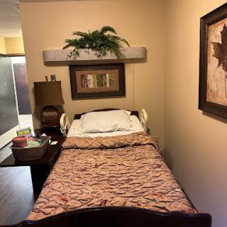 A cozy bedroom with a hospital bed, decorated with a floral bedspread and framed artwork on the walls.