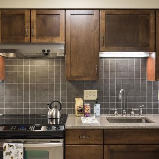 A cozy kitchen with wooden cabinets, a stainless steel stove and kettle, and a tiled backsplash.