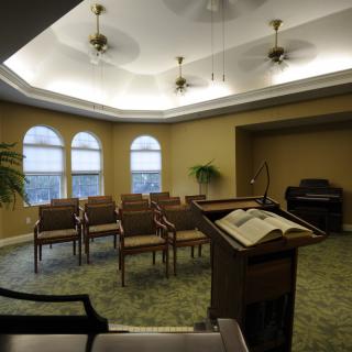A small chapel interior with chairs arranged facing a pulpit and an organ in the corner.