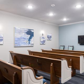 An interior view of a small room with wooden church pews, artwork on the walls, and ceiling lights.