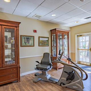 A well-decorated room featuring an exercise bike, framed artwork, and wooden display cabinets.