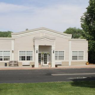 A small office building with a classic facade, surrounded by greenery under a clear sky.