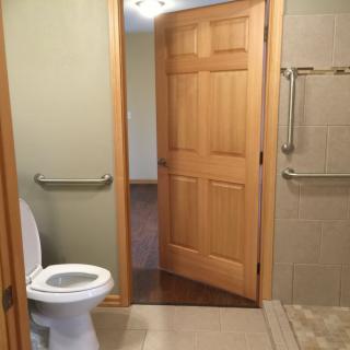 A bathroom with a toilet, wooden door, and grab bars near the shower.