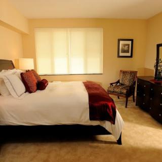 A cozy bedroom featuring a neatly made bed with red and white accents, a window allowing natural light, and classic wooden furniture.