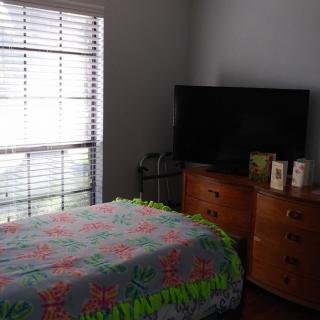 A cozy bedroom with a colorful bedspread, a large TV, and a dresser by the window.