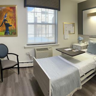 A modern and clean hospital patient room featuring a bed, chair, and artwork.