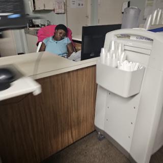 A person seated at a reception desk, working on a computer in an office environment.